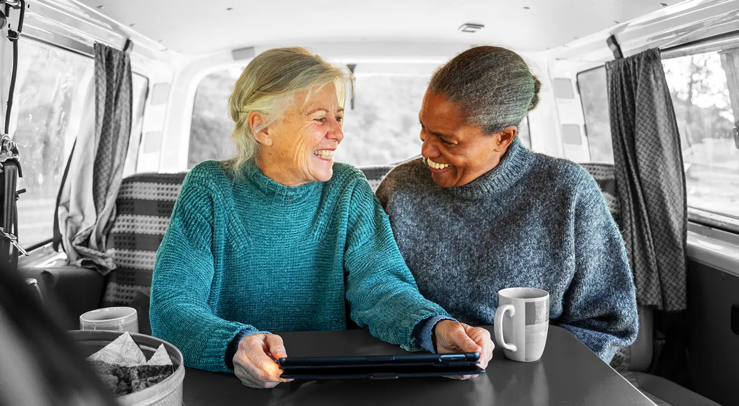 Two people sitting in a camper van, looking at a tablet together with a mug on the table.