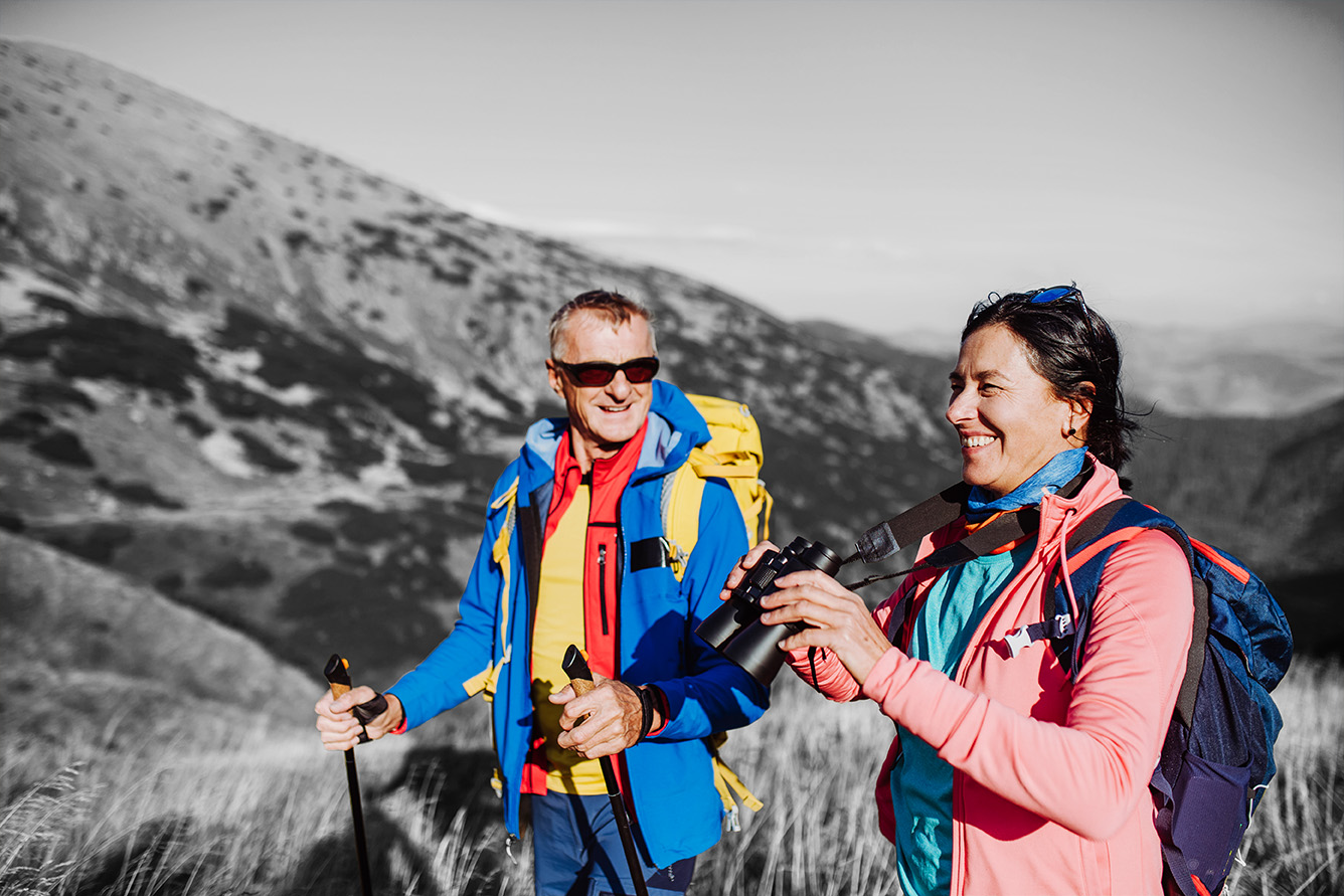 Two hikers with backpacks and walking poles on a mountain trail.