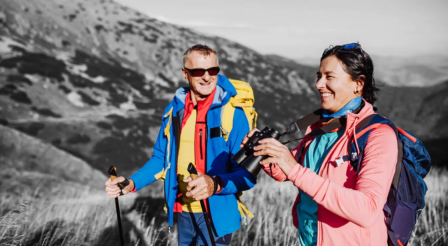 Two hikers with backpacks and walking poles on a mountain trail.