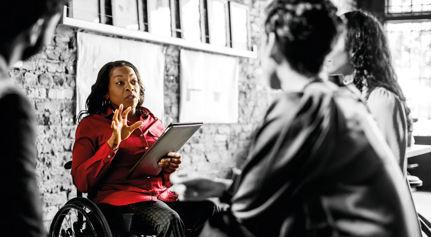 Professional leading a collaborative team discussion using a tablet in a workplace setting, highlighting communication, leadership, and inclusive working environments.