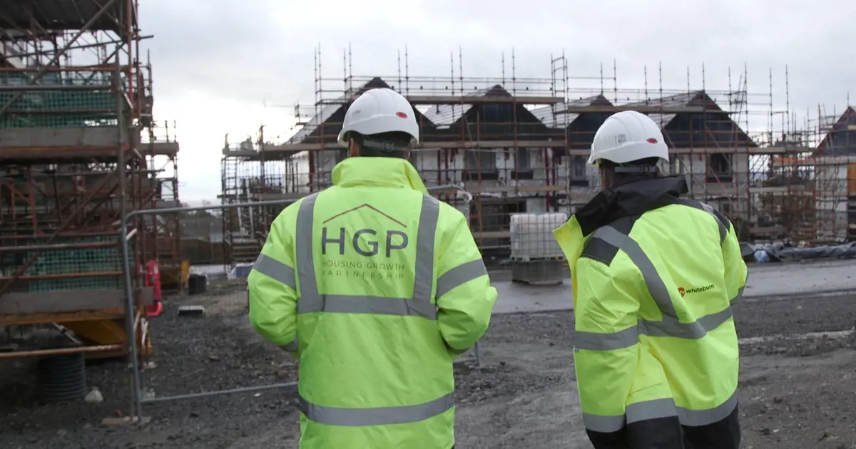Two Housing Growth Partnership employees in helmets and high visibility jackets looking at a housing development.