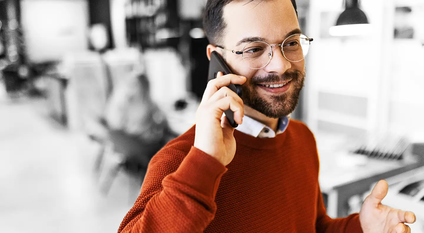 Person wearing glasses and an orange jumper talking on a mobile phone in a modern office.