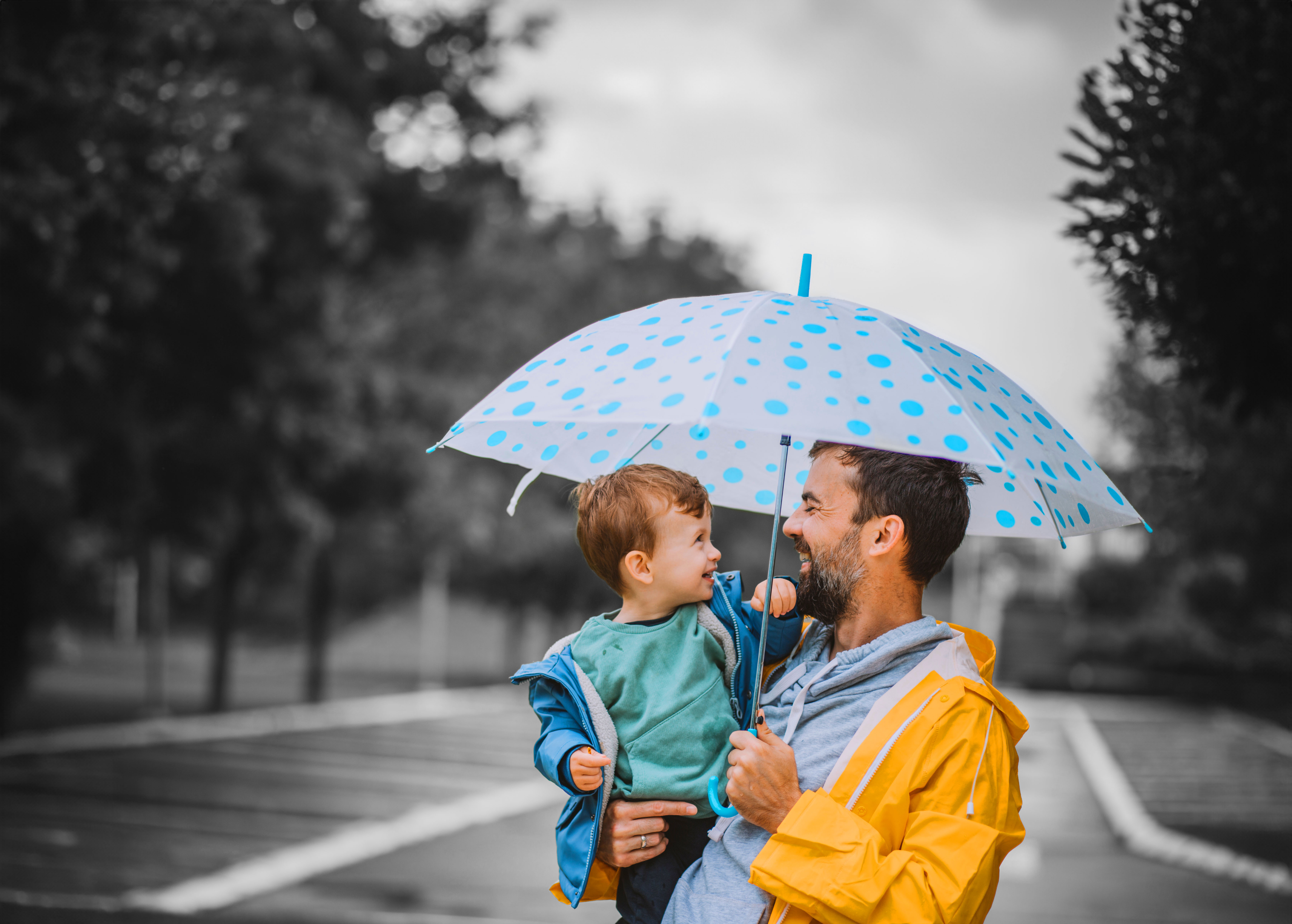 Person holding a child under a blue polka-dot umbrella on a rainy day.