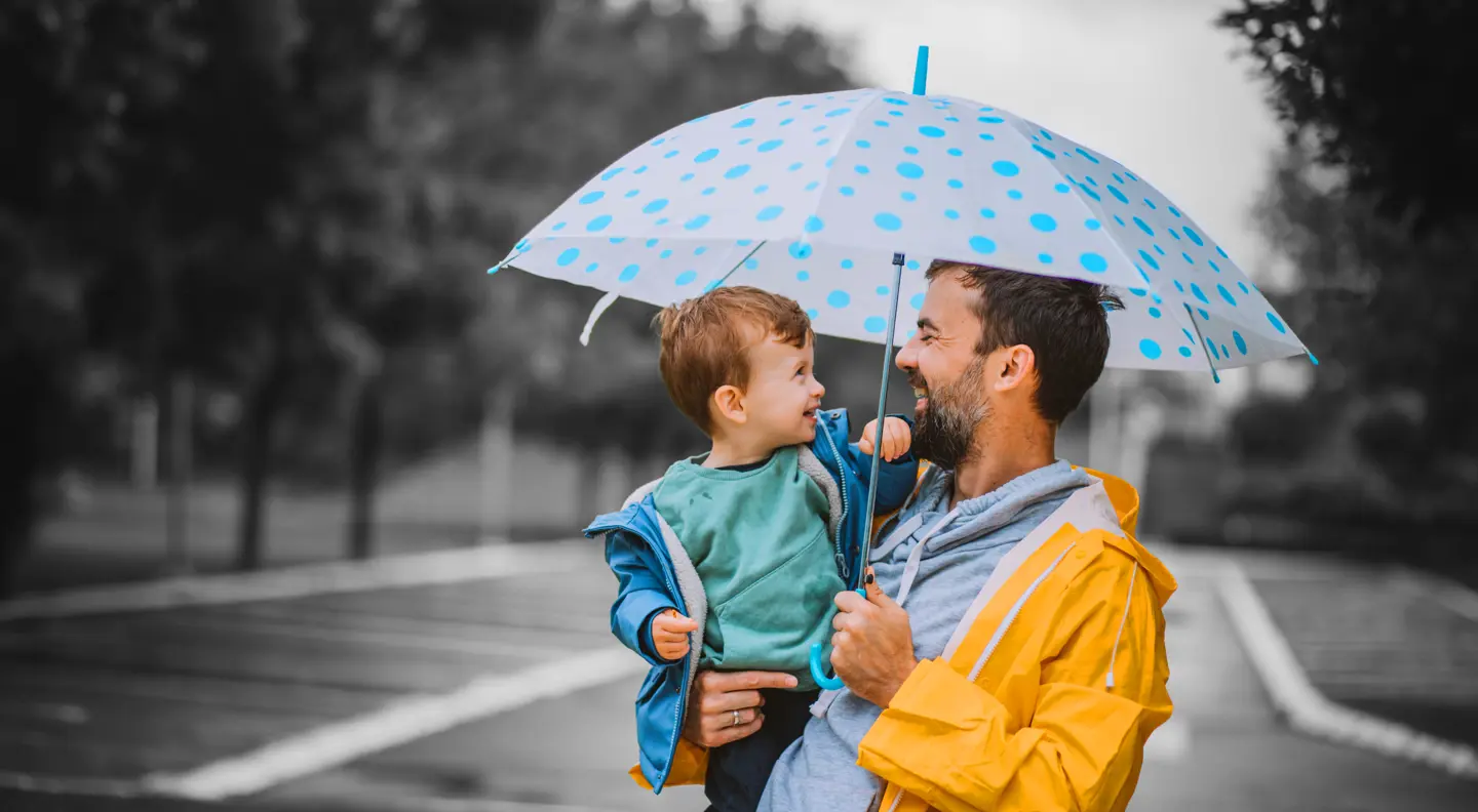 Person holding a child under a blue polka-dot umbrella on a rainy day.