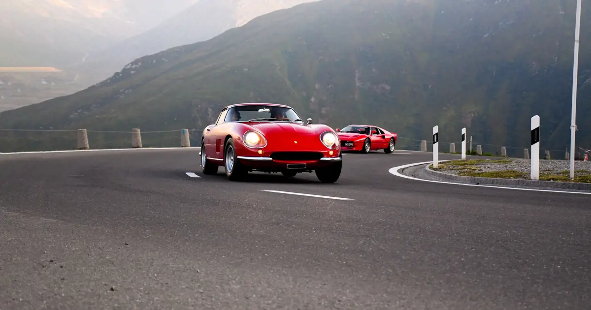 Two red cars driving up a mountain road.