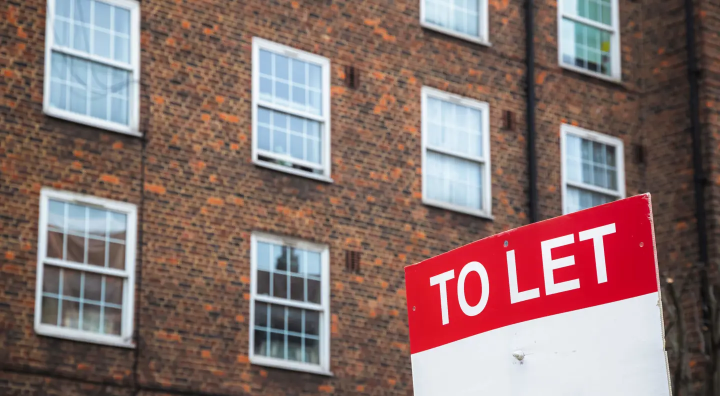 Exterior view of a brick apartment building with multiple windows and a red 'TO LET' sign displayed prominently.