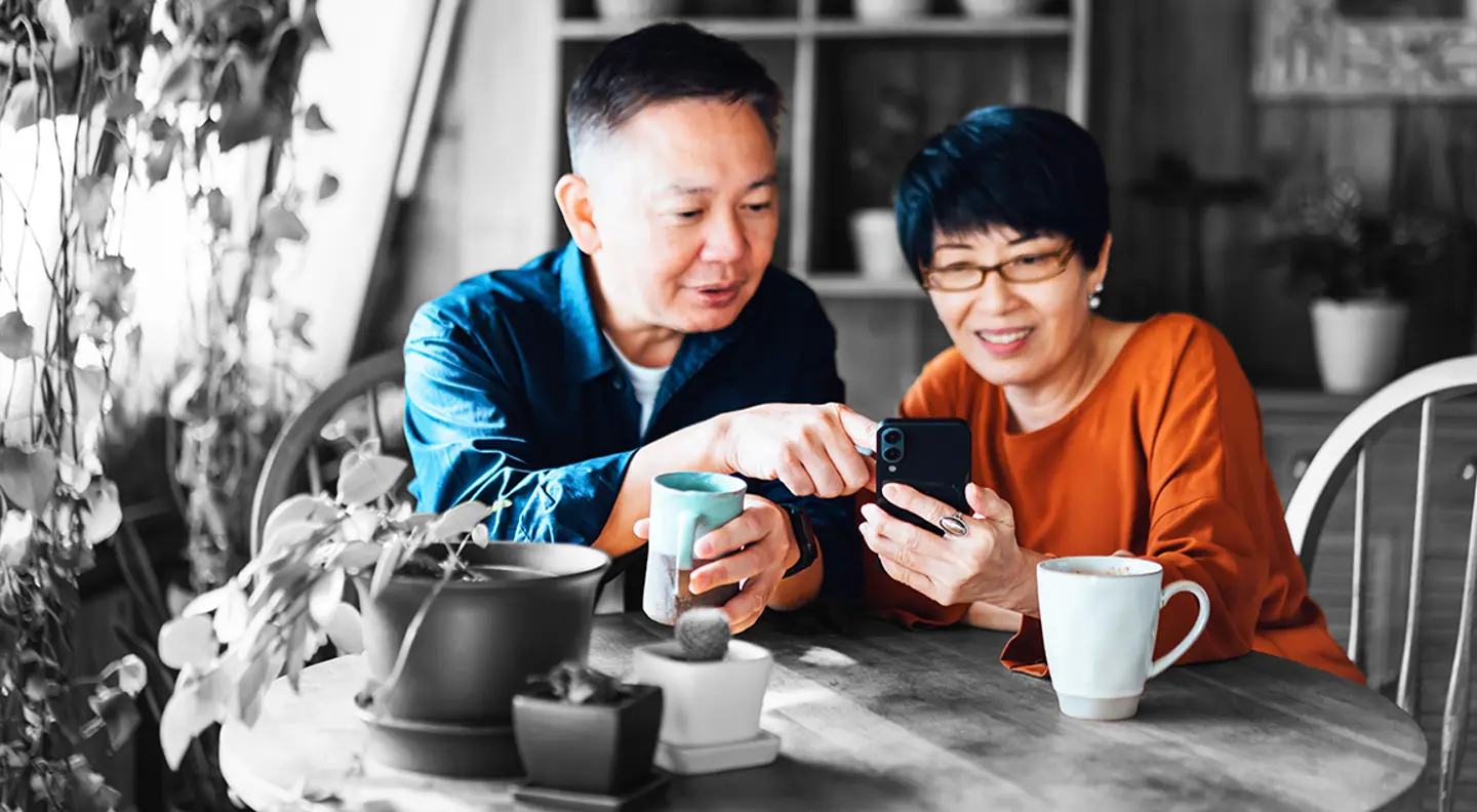 Elderly couple look at their phone at a coffee table